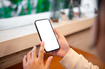 Close-up image of a woman using her smartphone while sitting by the window in a coffee shop.