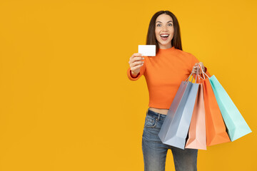 Young woman with paper bags and card on yellow background