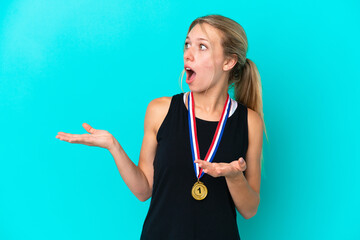 Young caucasian woman with medals isolated on blue background with surprise facial expression