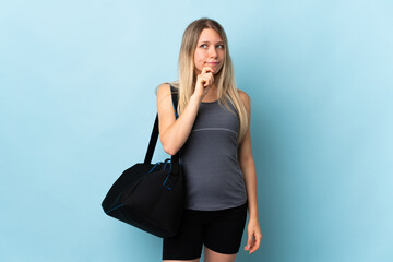 Young sport woman with sport bag isolated on blue background having doubts and thinking