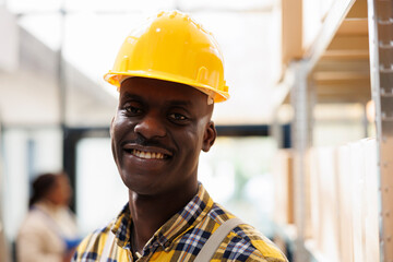 African american warehouse package handler in yellow helmet portrait. Industrial storehouse young...
