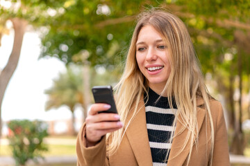 Young pretty blonde woman at outdoors sending a message or email with the mobile