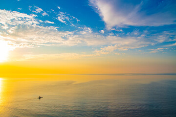Calm evening landscape with a small silhouette of a lonely man in a canoe. Sea at sunset. Summer background with empty space for text.