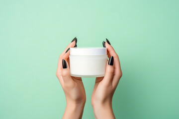 Female hands holding white cosmetics jar of face cream on green background. Beauty cosmetic product industry, skin care concept