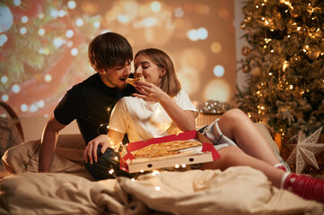 With pizza. Beautiful young couple indoors, celebrating new year against projector