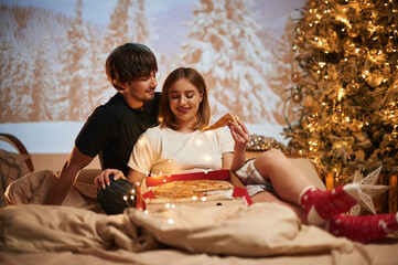 Delicious pizza. Beautiful young couple indoors, celebrating new year against projector