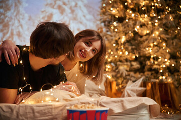 Cozy room with fir tree. Beautiful young couple indoors, celebrating new year against projector