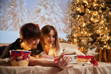 Taking photo by phone. Beautiful young couple indoors, celebrating new year against projector