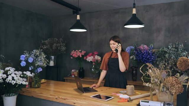 Seller, the owner of a flower shop, talks to the customer on the phone and takes an order for a bouquet on a laptop. Small business concept