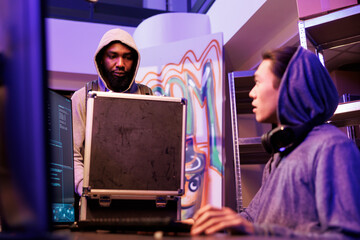 African american hacker opening black box with malicious ransomware program for data breach. Scammer showing case with illegal technology and planning hacking attack with crime partner