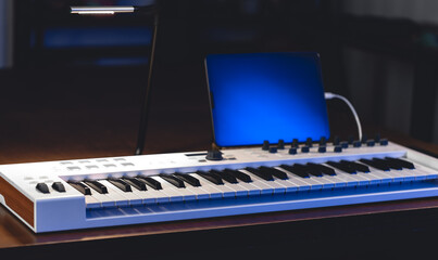 Musical keyboard and tablet in a dark room, music production.