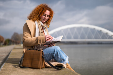 Caucasian ginger woman with freckles and curly hair is relaxing and reading a book.