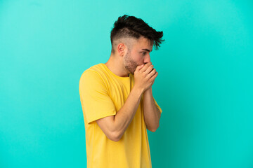 Young caucasian man isolated on blue background covering mouth and looking to the side