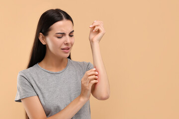 Suffering from allergy. Young woman scratching her arm on beige background. Space for text