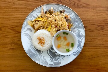 Indonesian food Ayam Geprek nasi served with traditional soup, rice, fried onion, and kremes put on wooden texture table