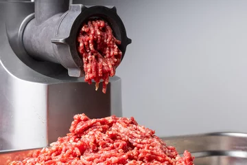 Fotobehang raw beef minced meat comes out of mincing machine mincer front view close up banners advertising © Maija
