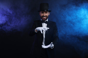 Happy magician holding something in smoke on dark background