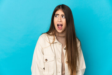 Young caucasian woman isolated on blue background doing surprise gesture while looking to the side