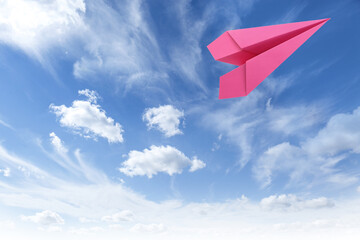 Pink paper plane flying in blue sky with clouds
