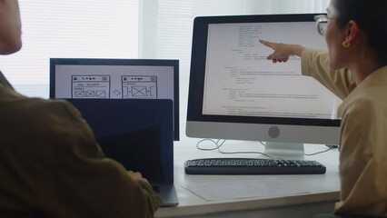 Back view of two developers testing new code following instruction while sitting in front of digital devices at workplace in office