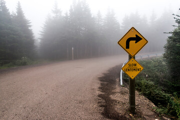 Slow Lentement sign Warning yellow roads signs road in Background foggy Cape Breton Island Nova...