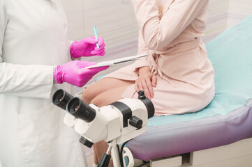 A young woman in a hospital gown at a gynecologist's appointment. A gynecologist wearing pink gloves writes a prescription to a patient. Gynecological microscope close-up
