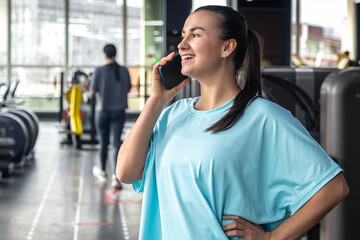 Happy young woman athlete talk on a phone at gym, copy space.