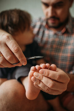Father cutting little boy's toe nails with scissors at home
