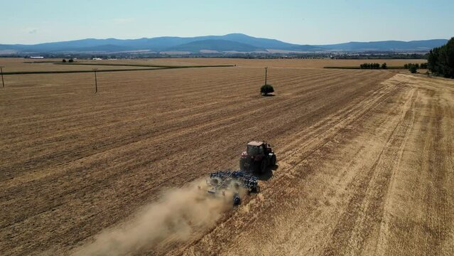 Tractor with harrow system plowing ground on cultivated farm field. Industrial 