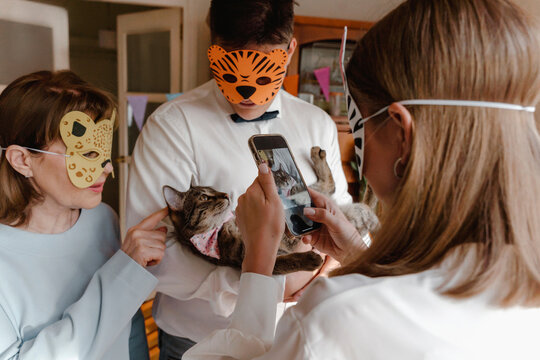 Family wearing animal masks and taking picture of cat through smart phone