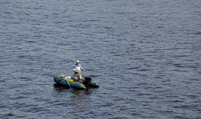 Mature man fishing on the lake from rubber inflatable boat. Fishing on the river. Natural river background