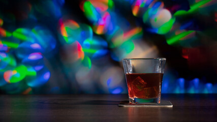Glass of whiskey on the bar in front of the blur image Christmas background. Festive abstract background with bokeh defocused lights and stars