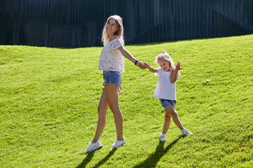 Mother with daughter walking on the lawn in the summer city park. Childhood, leisure and people concept - happy family rest and have a good time