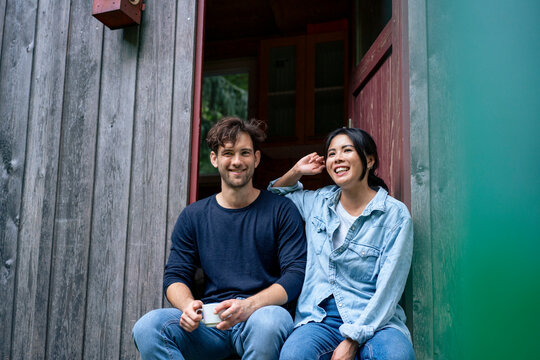 Happy man and woman sitting in doorway of log cabin