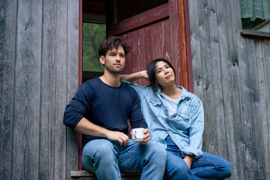 Young man and woman sitting in doorway of log cabin