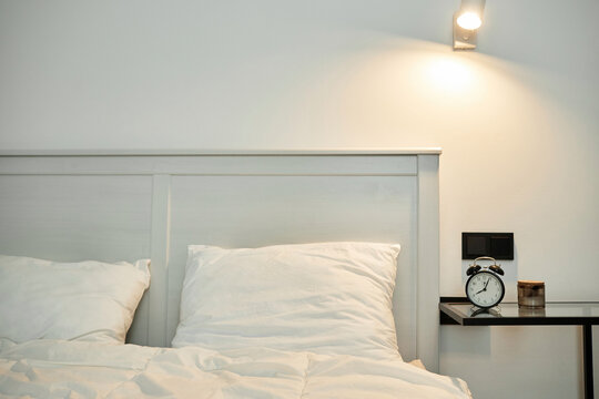 Bedroom interior, bed with white linen and bedside table with alarm clock on it