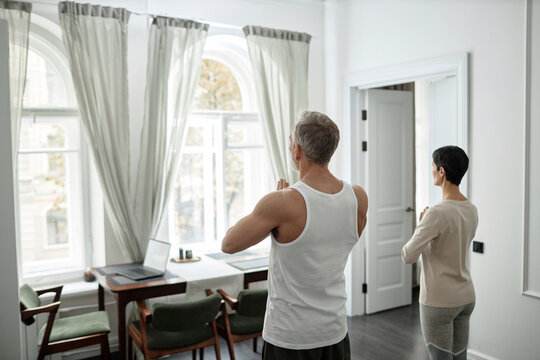 Rear view of adult couple folding palms in front of them during morning meditation at home