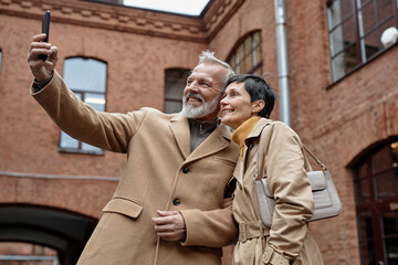Happy elderly couple taking selfie on smartphone during city walk