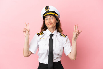 Airplane middle aged pilot woman isolated on pink background showing victory sign with both hands