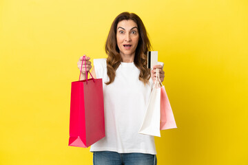 Middle aged caucasian woman isolated on yellow background holding shopping bags and surprised