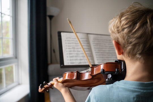 Boy practicing violin with sheet music at home
