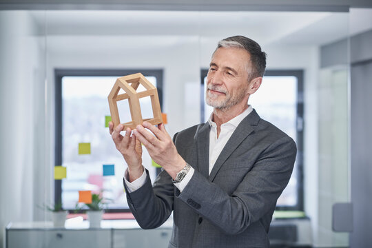 Smiling real estate agent examining model house in office 