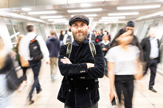 Man with arms crossed standing amidst people moving at subway station