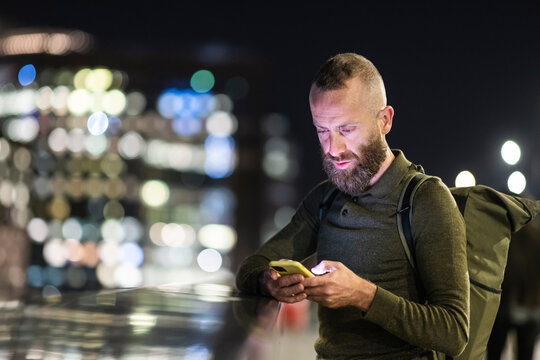 Man with beard using smart phone in city at night