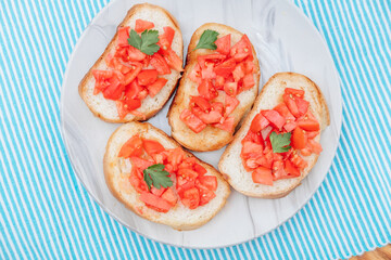 Delicious bruschetta, toasted bread with tomatoes on a plate, on a blue background, top view