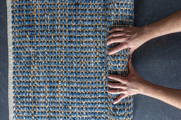 Man rolling hand woven geometric denim area rug on a wooden floor at home.