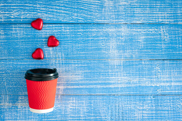 Red paper cup and heart-shaped candies on a blue wooden background.