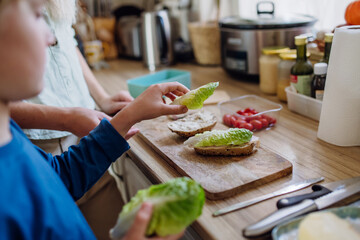 Boy helping mother to make school lunch in the kitchen. Preparing healthy snack for school.