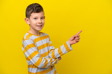 Little caucasian boy isolated on yellow background pointing finger to the side