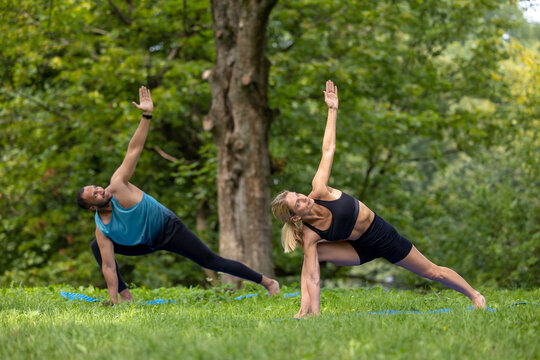 Man and woman doing yoga exercises in green park.